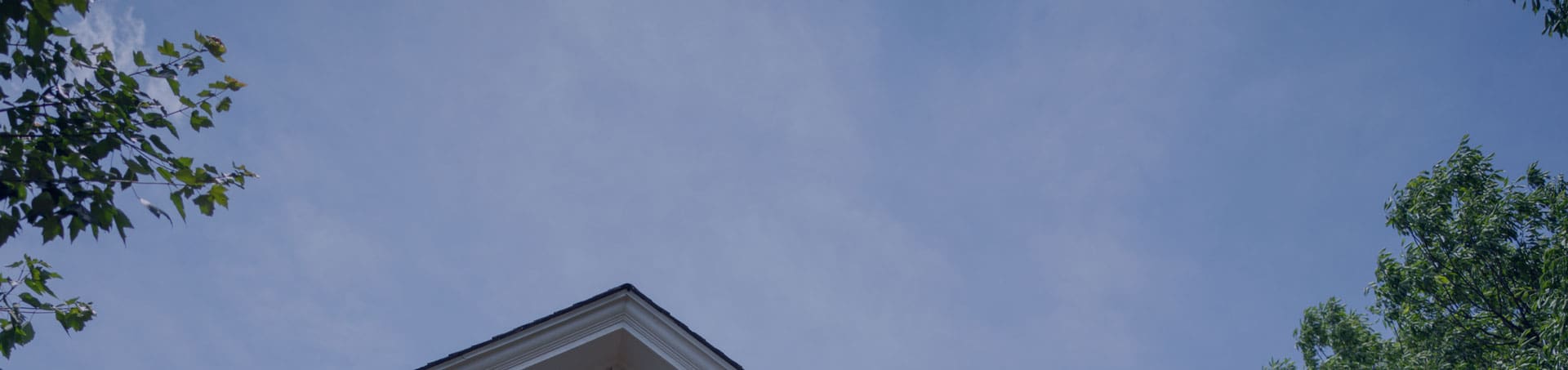 Blue sky with tree tops and the corner of a roof showing.