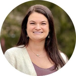 Nurse Practitioner Eva Rellins wears a brown top and light beige cardigan in front of a wooded background.