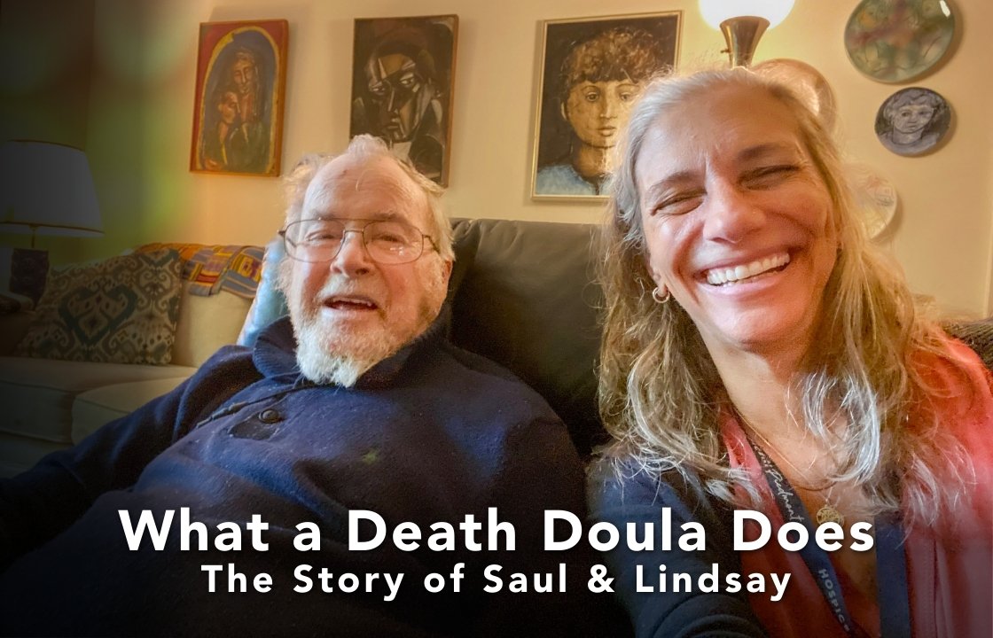 A Palliative Medicine Patient in a navy blue sweater sits beside a Death Doula with a salmon scarf. The smile. In the background, we see the patient's artwork.